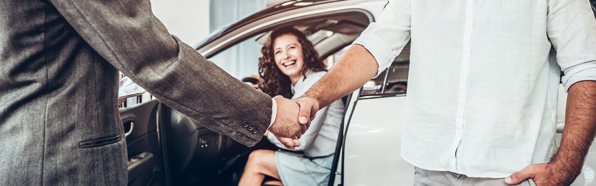 young woman in car while two men shake hands
