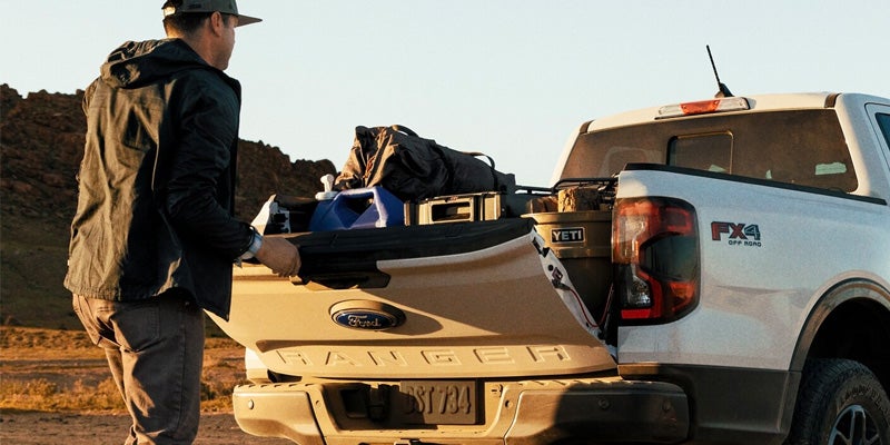Man unloading gear from a Ford Ranger truck outdoors.