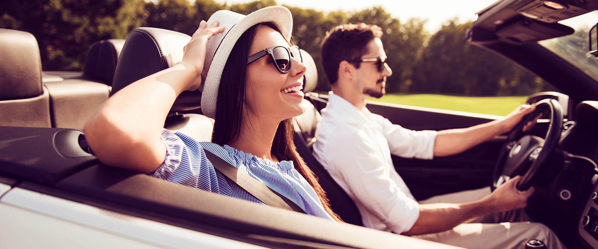 man driving car and woman with hat sitting besides