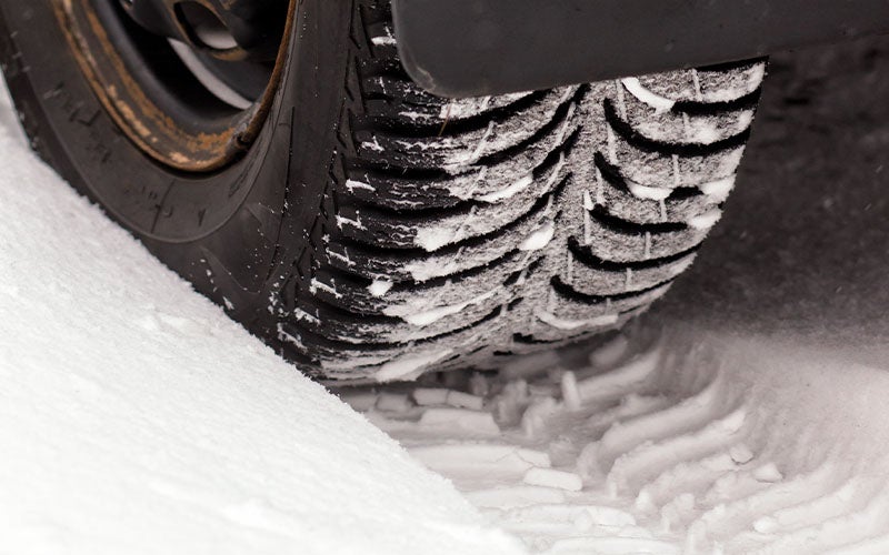 Car tire with deep tread driving on snow, leaving a clear track.